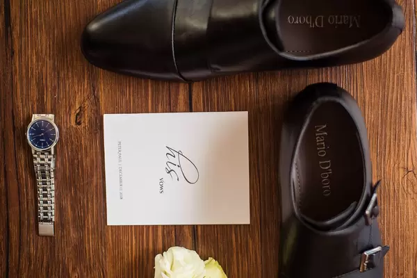 Bereitgelegte Accessoires für den Bräutigam mit eleganten Schuhen, silberner Uhr und weißer Rose