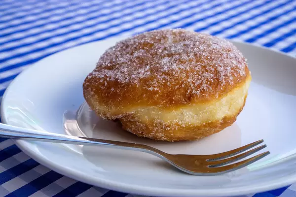 Berliner Pfannkuchen mit Vanillecreme und Zucker auf einem Teller mit einer Gabel Nahaufnahme