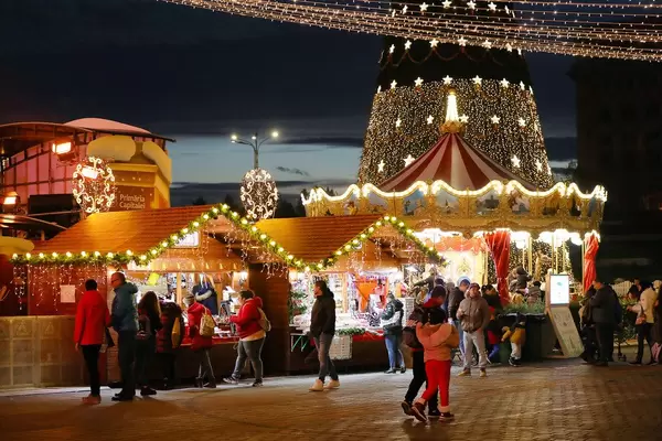 Besucher und beleuchtete Hütten auf dem Weihnachtsmarkt in Bucharest, Rumänien, Nachtsaufnahme