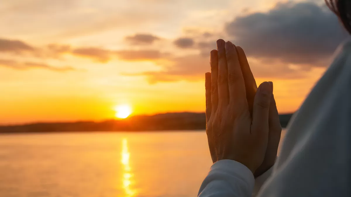Betende Hände im Sonnenuntergang am Wasser