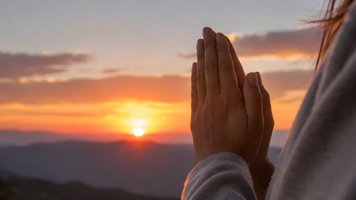 Betende Hände vor orangenem Sonnenuntergang in Bergen