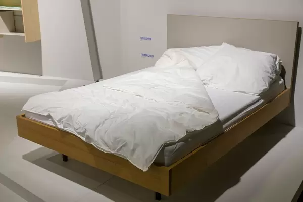 Bett mit Holzrahmen, Kissen und Decke in Ausstellungsraum