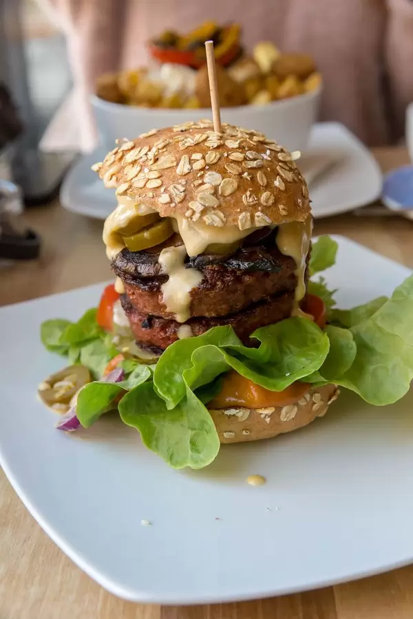 Beyond Meat Burger with fresh vegetables and Ketchup Special on a white plate with a vegan falafel meal in the background