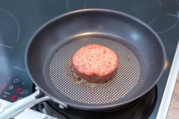 Beyond Meat Patty - the vegan alternative of burger meat - is being fried in a frying pan on an induction stove