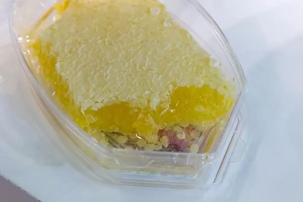 Bienenwabe in einem transparenten Plastikbehälter auf weißem Hintergrund