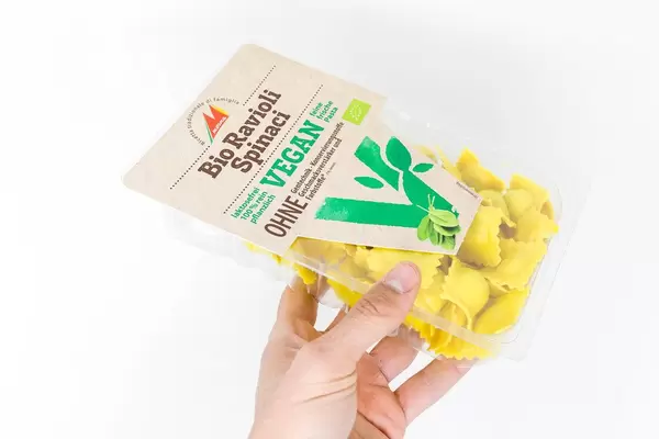 Bio, vegan und laktosefrei: Hand hält Ravioli mit Spinat von Mosna in transparenter Verpackung vor weißem Hintergrund