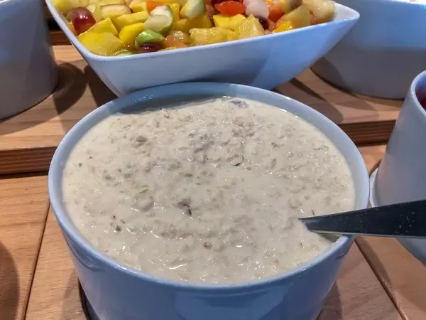 Bircher Müsli Porridge, Haferbrei, in einer weißen Schüssel, vor einem Obstsalat