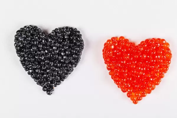 Black and red caviar hearts on white, top view