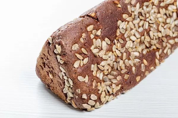 Black bread with sunflower seeds on white wooden background