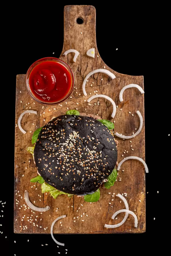 Black burger with cutlet, onion, sesame seeds and tomato sauce on an old wooden kitchen board, top view
