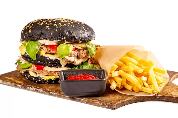 Black burger with meat cutlet and vegetables on a wooden board with french fries