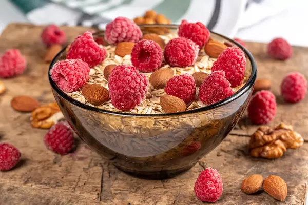 Black glass bowl with oatmeal, raspberries and almonds on an old wooden board