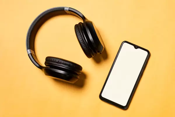Black music headphones and smartphone on yellow background