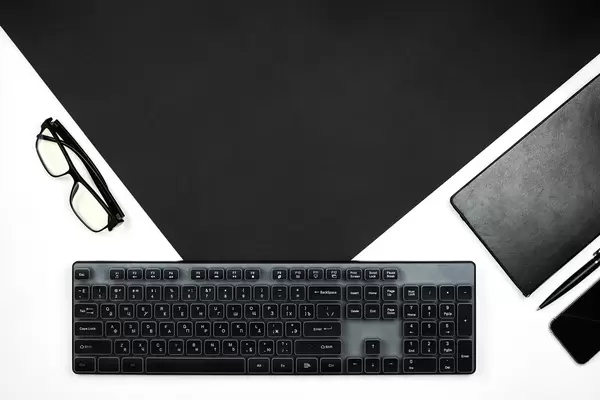 Black pc keyboard, notepad, eyeglasses and smartphone on black and white surface