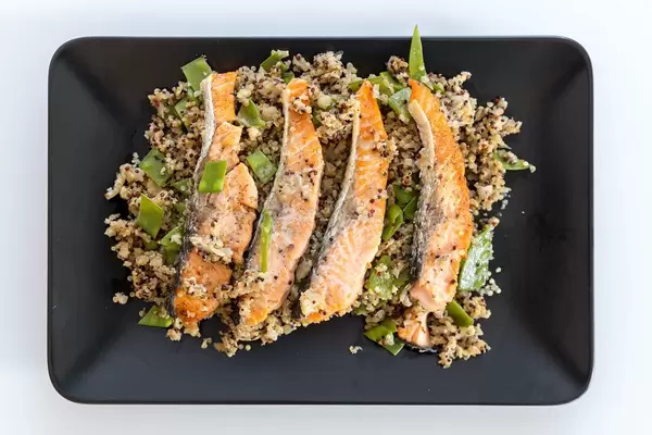 Black plate with beautifully arranged salmon stew with cauliflower quinova and parmesan