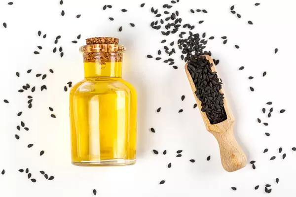 Black sesame seed and a bottle of sesame seed oil over white background, top view