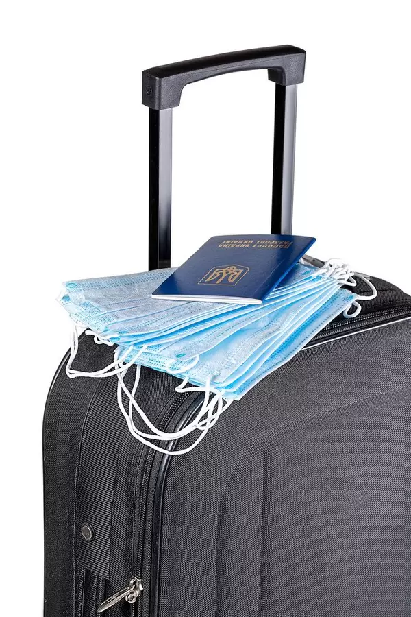 Black suitcase with a stack of medical masks and a passport