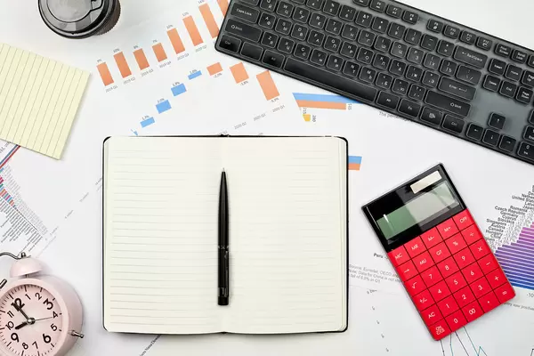 Blank notepad with financial graphs, calculator, alarm clock and keyboard on the workplace