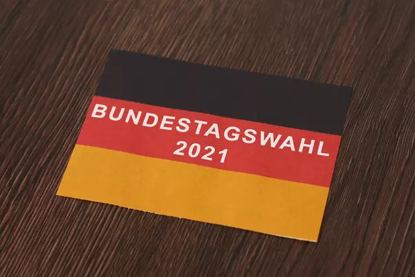 Blatt in den Farben der deutschen Flagge mit Schrift "Bundestagswahl 2021" auf hölzernem Hintergrund