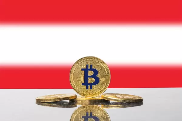 Blau-goldene Bitcoin-Münzen mit der rot-weißen Flagge Österreichs im Hintergrund