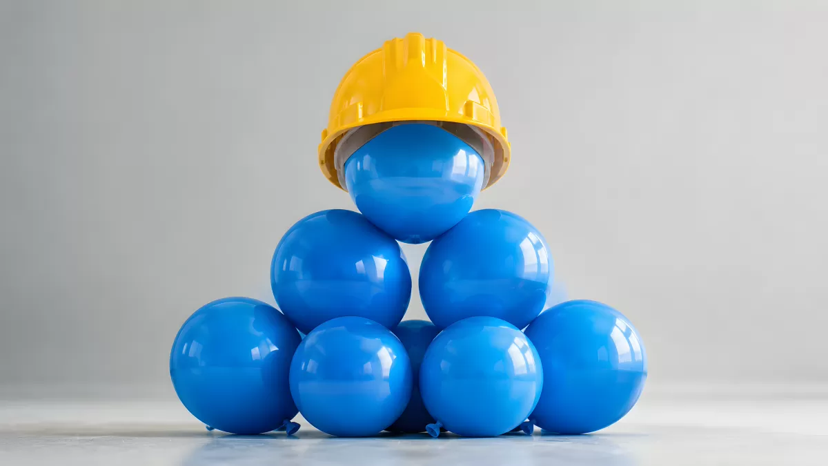 Blaue Luftballons als Pyramide mit gelbem Schutzhelm