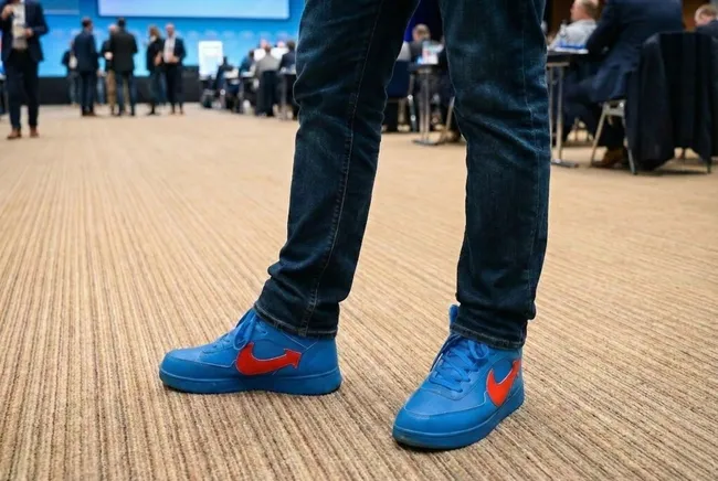 Blaue Sneaker mit rotem Logo auf Konferenzparkett