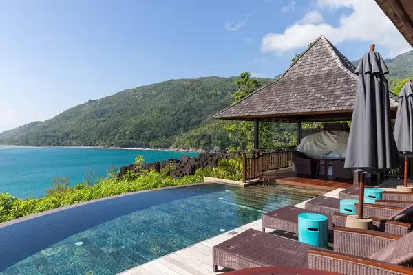 Blauer Infinity Pool und Sonnenliegen aus Rattan des Constance Ephelia Resort mit Blick auf den Indischen Ozean und Morne Nationalpark auf Mahé
