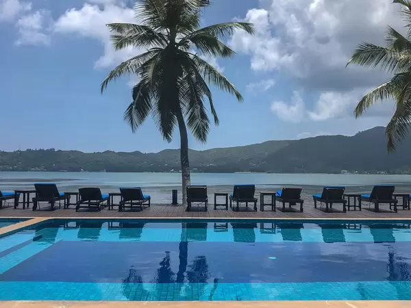 Blauer Pool mit Liegestühlen unter Palmen des "Iles des Palmes" Hotels, Blick auf Baie Sainte Anne der Seychelleninsel Praslin