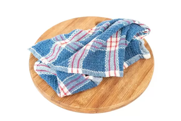 Blaues Geschirrtuch auf einem runden Küchenbrett vor weißem Hintergrund