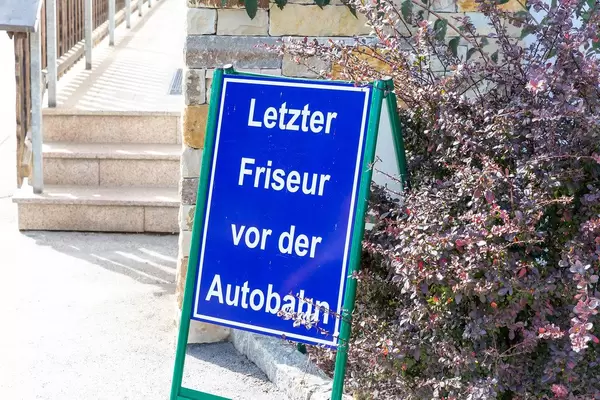 Blaues Schild "Letzter Friseur vor der Autobahn" in den Alpen in Österreich