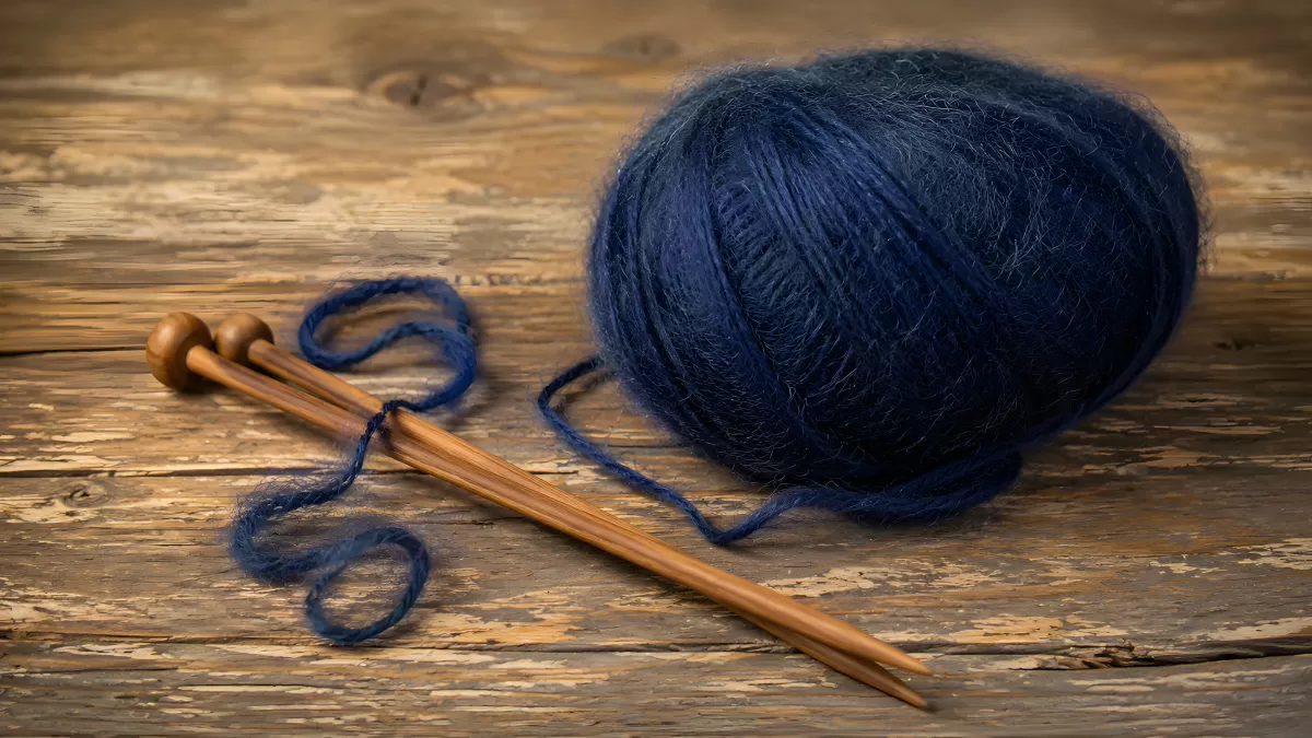 Blaues Wollknäuel mit Holzstricknadeln auf Holz