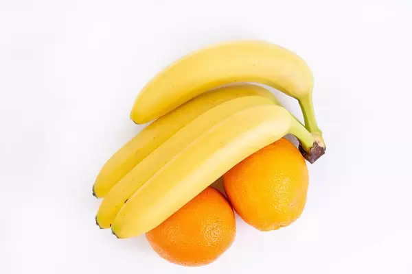 Blick auf reife Bananen und zwei Orangen, auf einer weißen Oberfläche