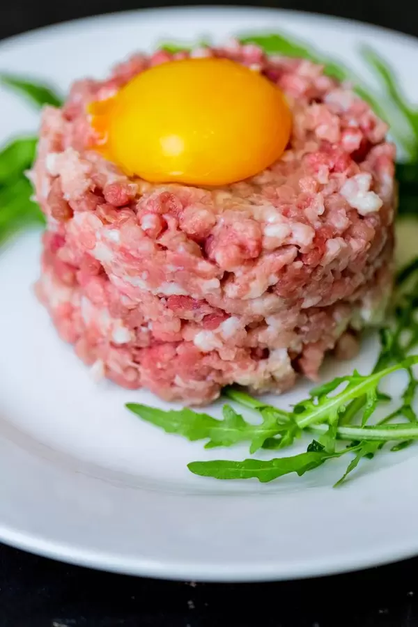 Blick auf Tatar Arugula mit rohem Eigelb und Rucolablättern auf weißem Teller
