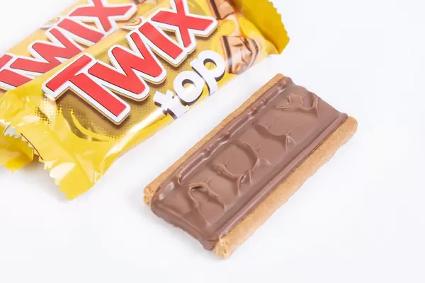 Blick auf Twix Top in Verpackung sowie ausgepackten Schokoriegel auf weißem Tisch