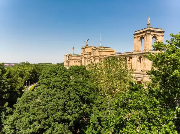 Blick über Baumkronen auf das imposante Gebäude des Bayrischen Landtags in München