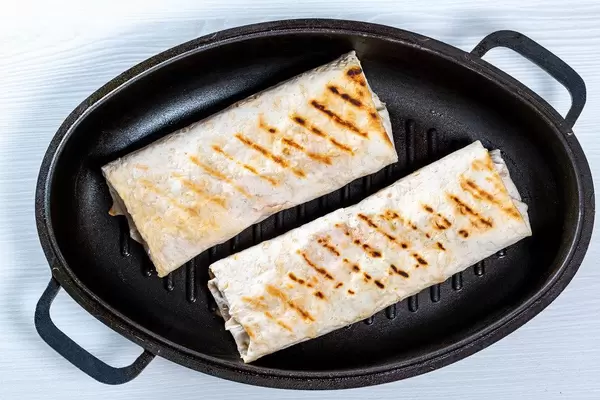 Blick von oben auf Bratpfanne mit zwei gebratenen Shawarma auf weißem Küchentisch