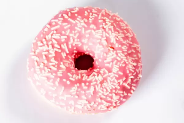 Blick von oben auf Donut mit pinkfarbener Glasur und weißen Streuseln vor weißem Hintergrund
