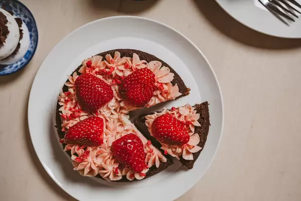 Blick von oben auf eine Nachspeise und angeschnittenen Erdbeerkuchen, mit rötlicher Sahnecreme