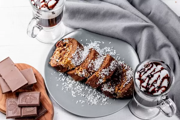 Blick von oben auf eine Schweizer Rolle aus Schoko und Kirsche, neben einer zerbrochenen Schokoladentafel und Kaffee mit Sahne