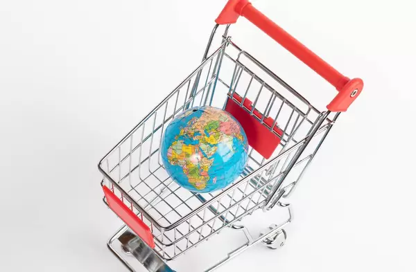 Blick von oben auf Einkaufswagen mit Weltkugel mit farbig hinterlegen Ländern vor weißem Hintergrund