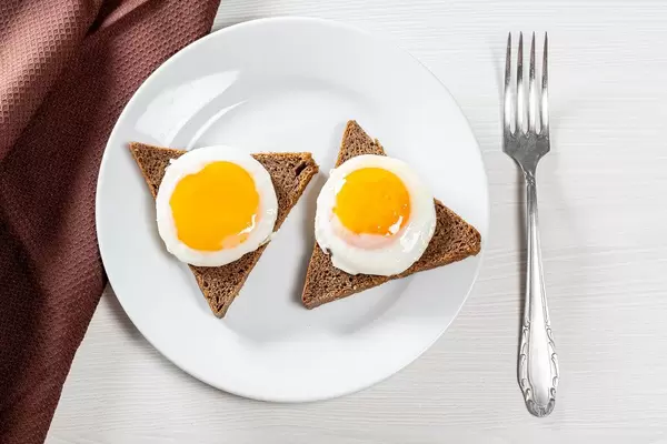 Blick von oben auf Frühstück mit zwei runden Spiegeleiern auf Toast auf weißem Tisch