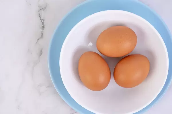 Blick von oben auf Frühstücksschale mit drei hartgekochten Hühnereiern auf grauem Marmortisch
