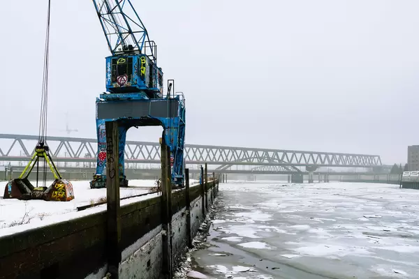 Blue abandoned port crane covered in Graffiti on the loading dock with frozen water below