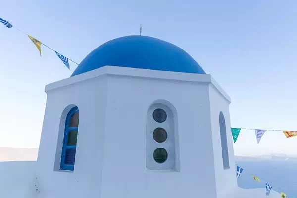 Blue and white in a typical Santorini picture of the famous church with a blue dome and triangular flags