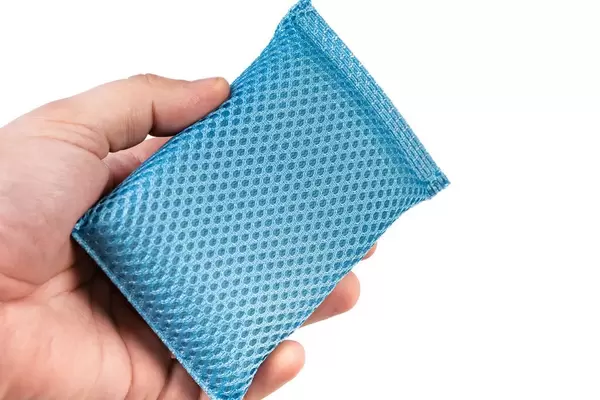 Blue dish washing sponge in the hand above white background