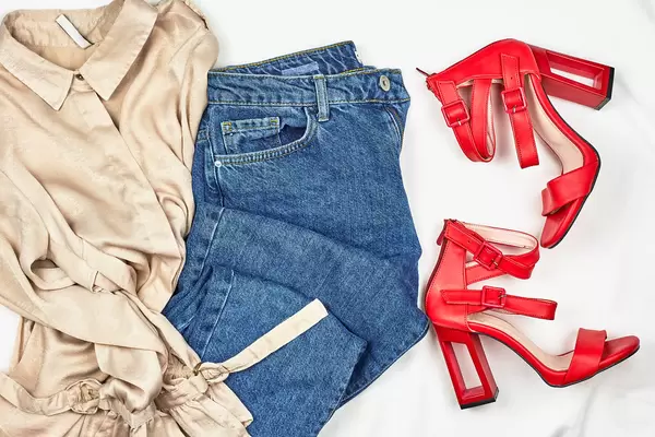 Blue jeans, pastel-colored shirt, and stylish female red shoes on white