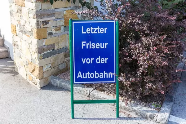 Blue sign in German "Last hairdresser before the motorway" in a village in the Austrian Alps