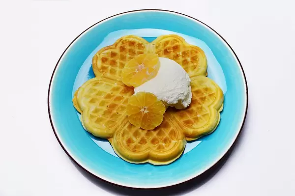 Blumenförmige Waffel aus fünf Stücken in Herzform, dekoriert mit Schlagsahne und Orangenscheiben