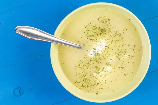 Blumenkohlsuppe mit Sauerrahm in einer gelben Schüssel auf einem blauen Holztisch