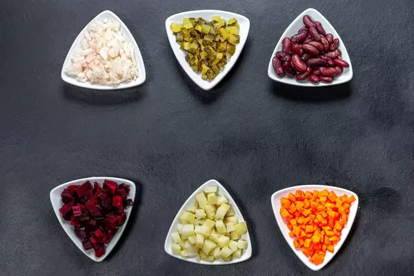 Boiled carrots, potatoes, beets, beans with pickled onions and cucumbers diced in triangular plates on a black background. The concept of cooking (Flip 2019)